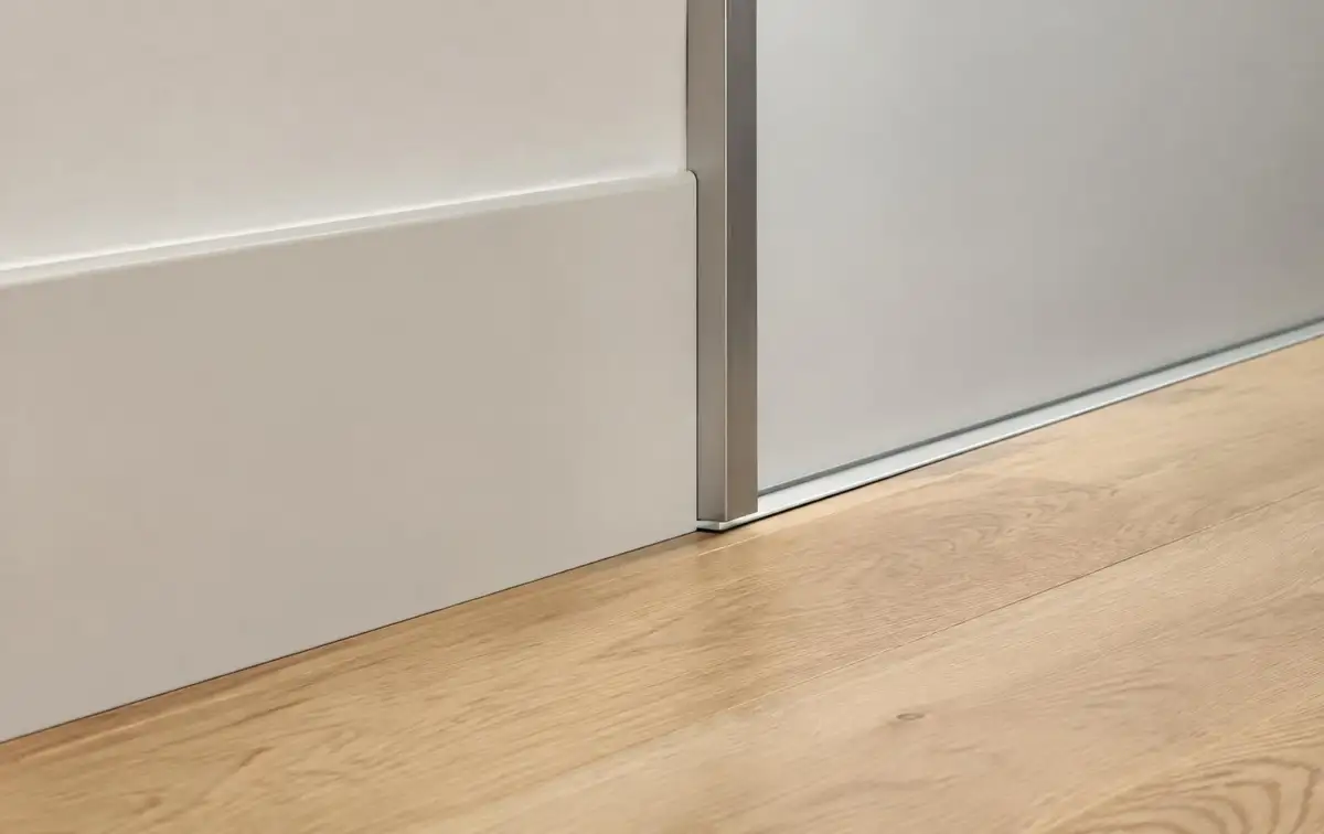 Tall white skirting board and slim aluminium profile meeting an oak floor